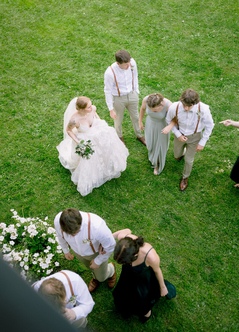 Aerial view of a bride and groom standing on grass with guests around them.