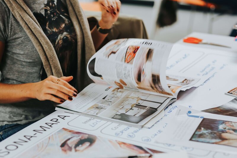 faceless person in a studio working at a cluttered desk while thumbing through a magazine