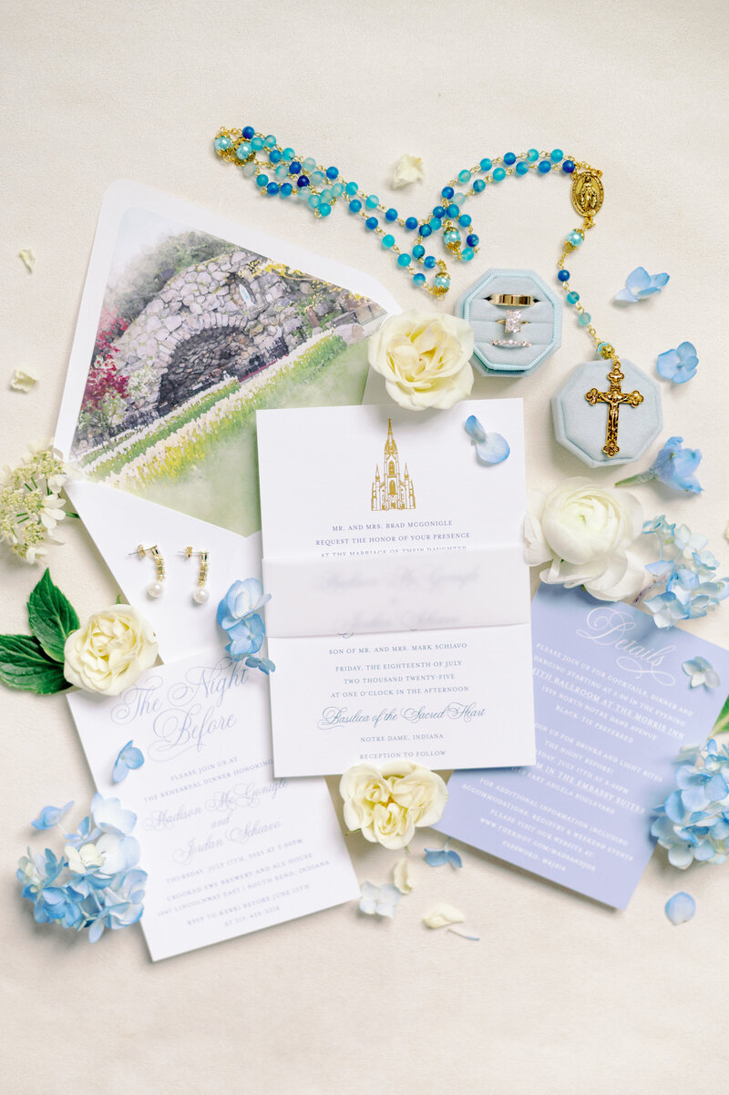 a wedding invitation suite surrounded by wedding details including a Catholic rosary and flowers