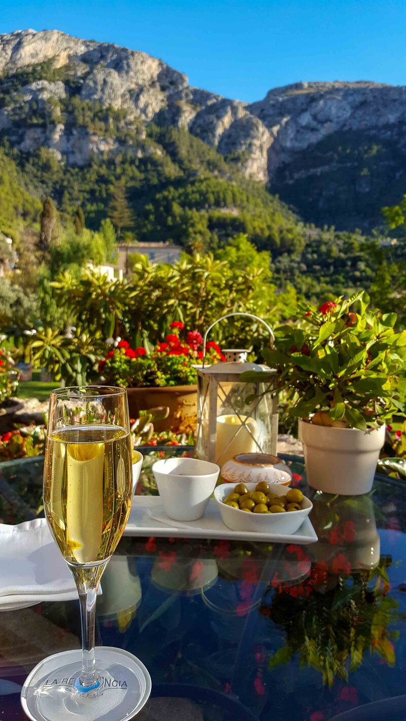Outdoor table set with a glass of cava, olives, and candlelight at Belmond La Residencia in Mallorca, with the Tramuntana Mountains in the background ©Stephanie Dosch | theViatrix Bespoke Spain Travel Planning