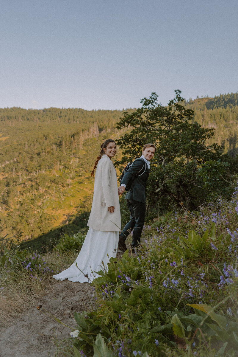 Bride and groom hiking up trail with wildflowers