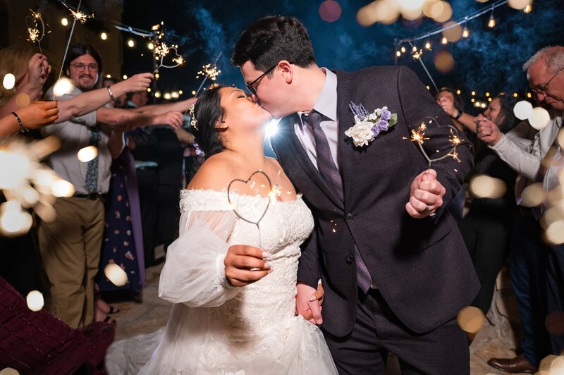 Bride and groom share a kiss while holding heart shaped sparklers during their wedding sendoff.