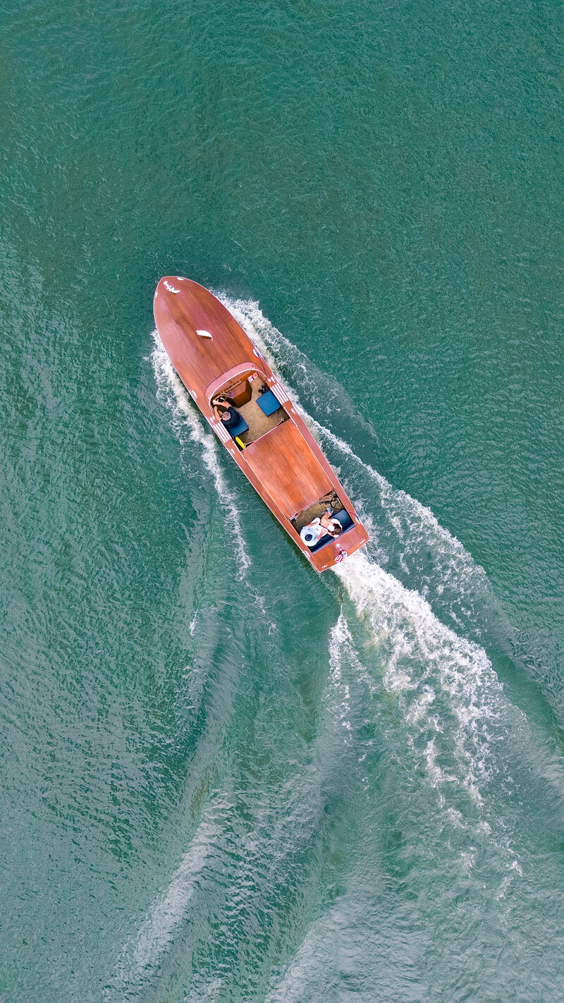 Engaged couple rides in a wood boat across the teal blue waters at Reynolds Lake Oconee