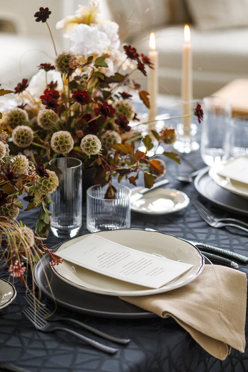 Modern, chic wedding reception table set with black and cream dishes, matte black flatware, and wave-textured glassware