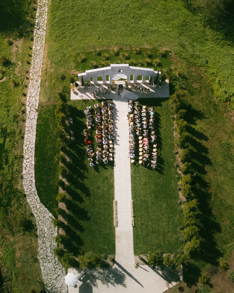 Groom wearing pink suit hugging and kissing bride on cheek from behind