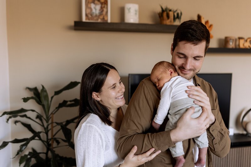 Mutter und Vater stehen im Wohnzimmer und Vater haelt Baby auf dem Arm