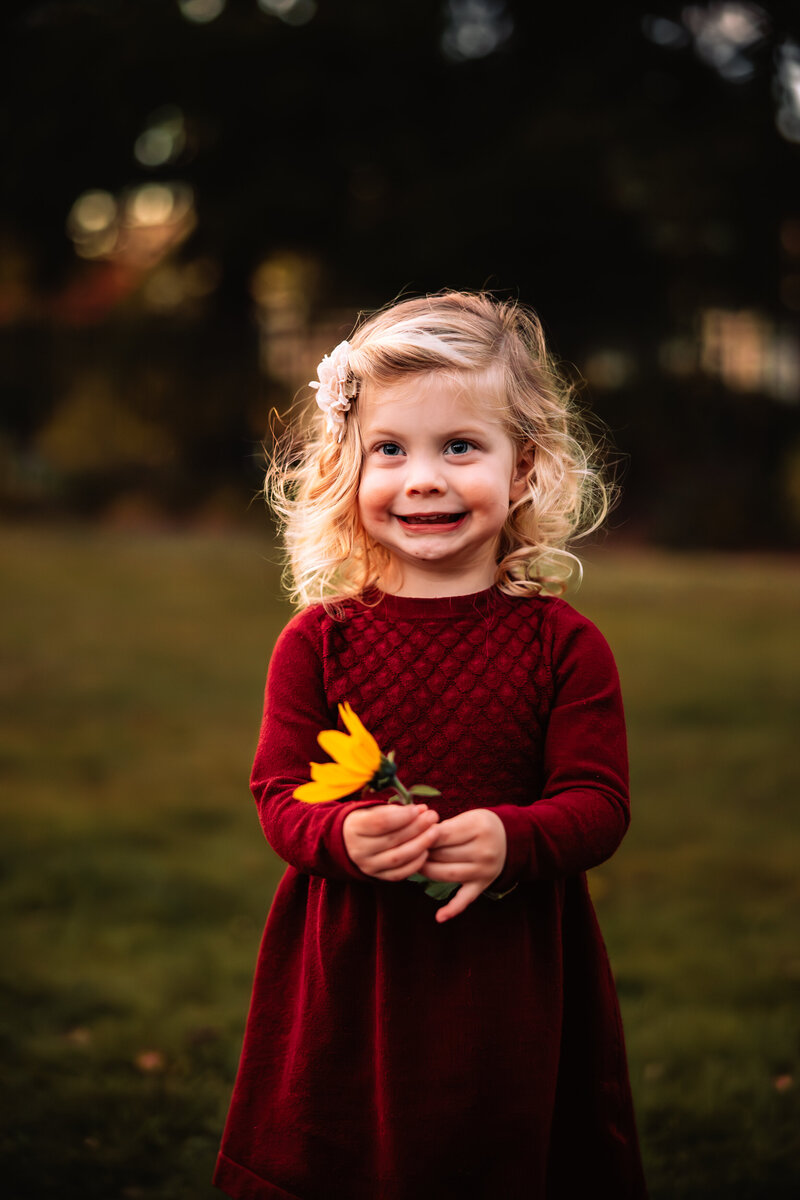 sunset backlit image of your girl smiling holding a flower with vibrant tones