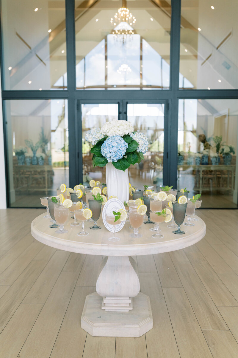Elegant wedding cocktail display featuring hydrangea centerpieces, vintage glassware, and refreshing lemonade spritzers garnished with lemon and mint at a refined Southern garden celebration.