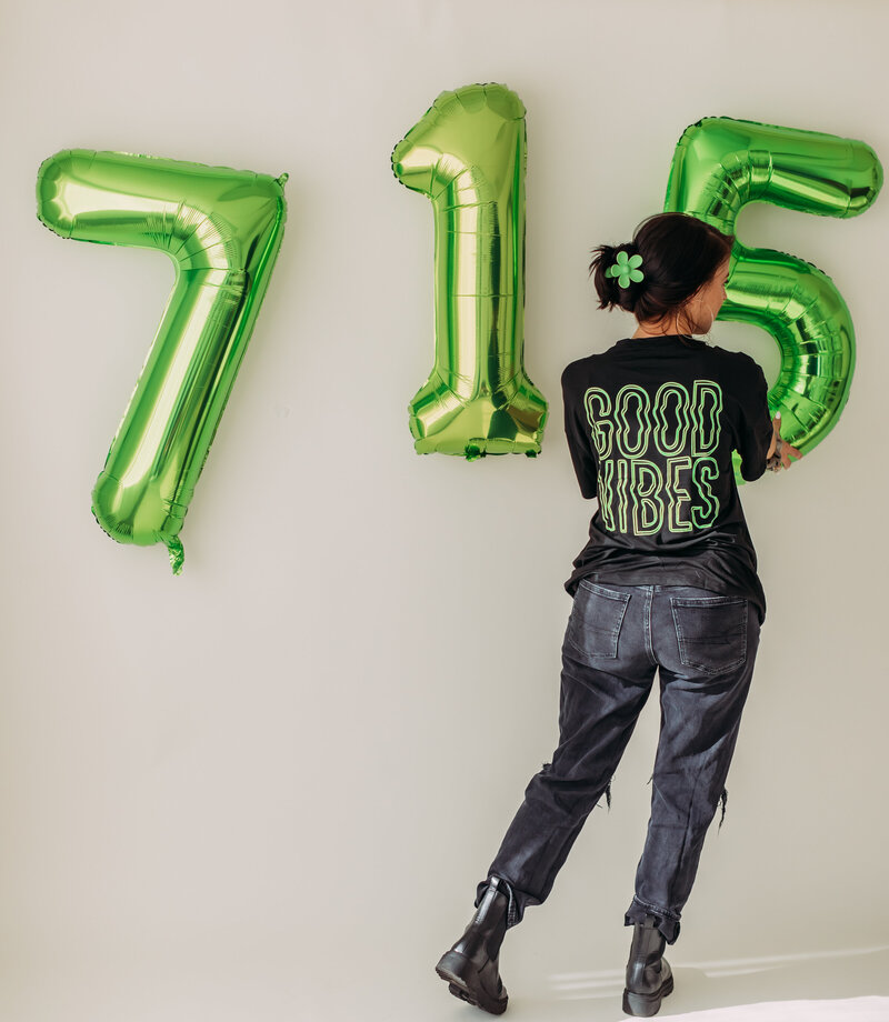 branded photo shoot for studio seven fifteen holding up 715 balloons with a t shirt that says good vibes