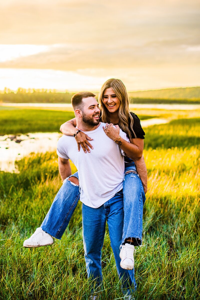 guy giving girlfriend piggyback ride in grass at Lake Mary in Flagstaff at golden hour engagement 