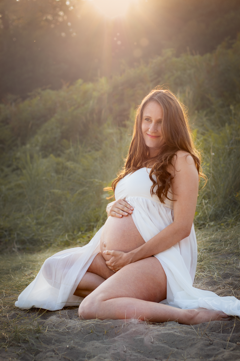 Pregnant lady sits on the sand cradling her baby bump