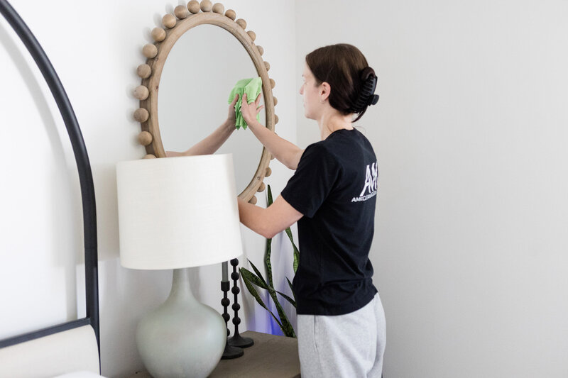Professional cleaner wiping down a mirror in a bedroom.