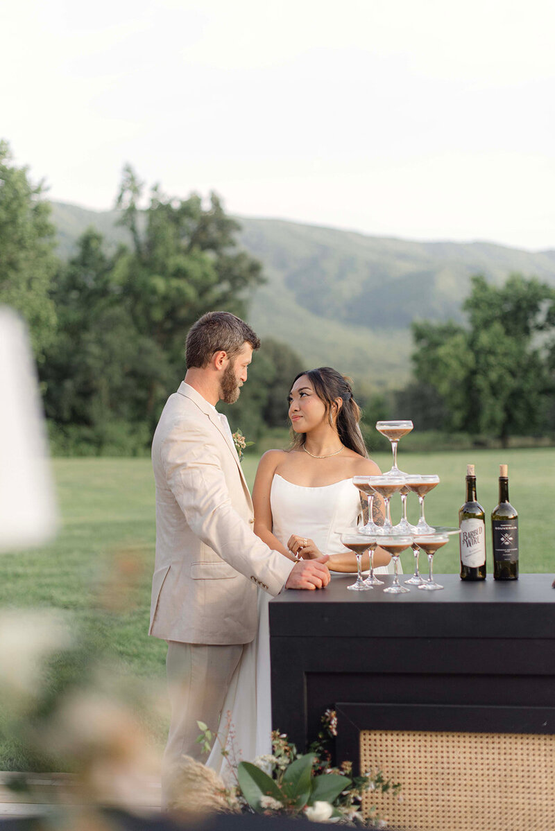 New bride and groom standing attentively at the bar setup on their wedding day, as they gaze into eachother's eyes with love