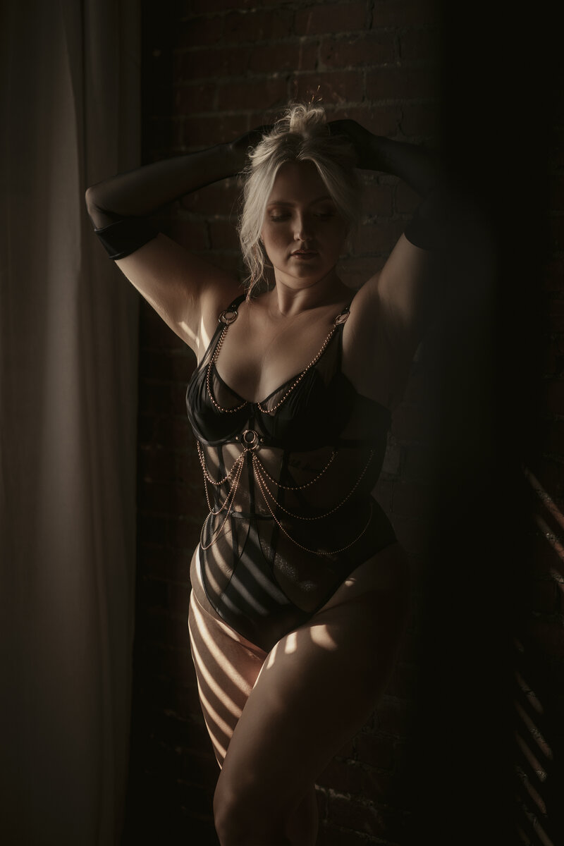 Boudoir portrait of a woman with long hair posing on a bed wearing black lingerie