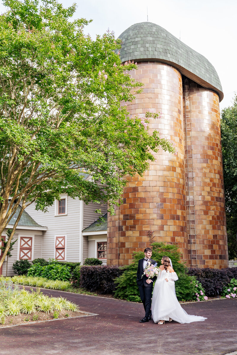 bride and groom walk in front of the silos at a wedding at the Historic Wakefield Barn in Raleigh, NC