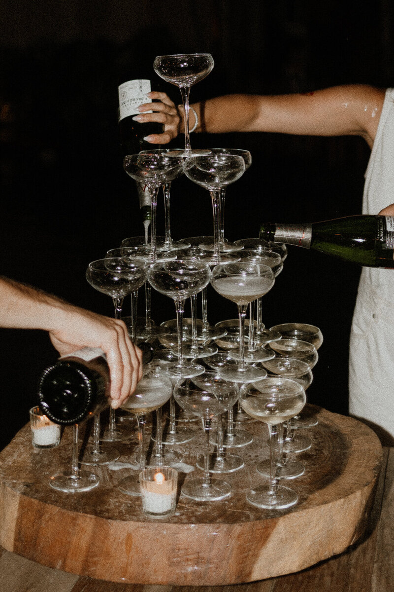 flash photo of couple pouring champagne into champagne tower at wedding reception in tulum mexico