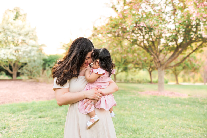 A mother and baby in a scenic field with blossom trees during a spring family photography session.