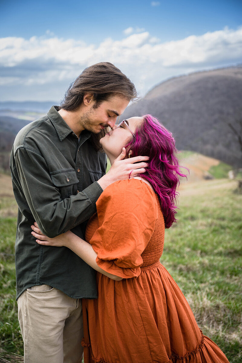 A couple go in for a kiss and hold onto one another atop of a Virginia mountain for their anniversary portrait adventure session.