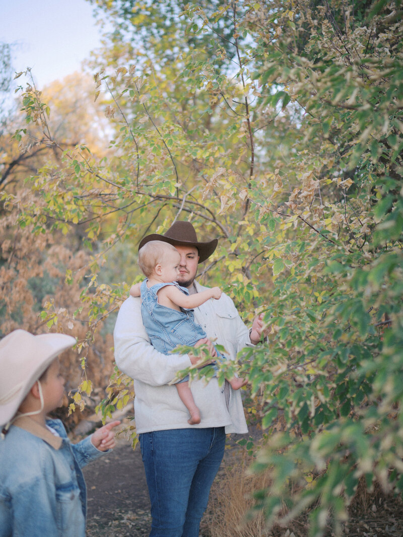 Father holding his son while showing him some leaves on a tree