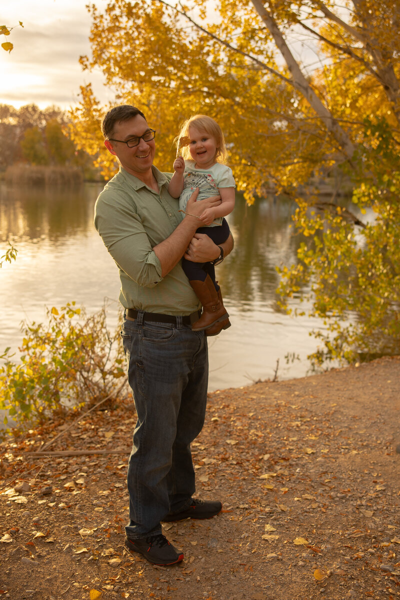 dad is holding his young daughter who is showing off a leaf in front of a pond at las vegas park floyd lamb park with alexis dean photography