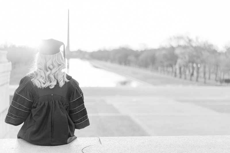 college girl sitting wearing graduation cap & gown during senior pictures at Washington Monument
