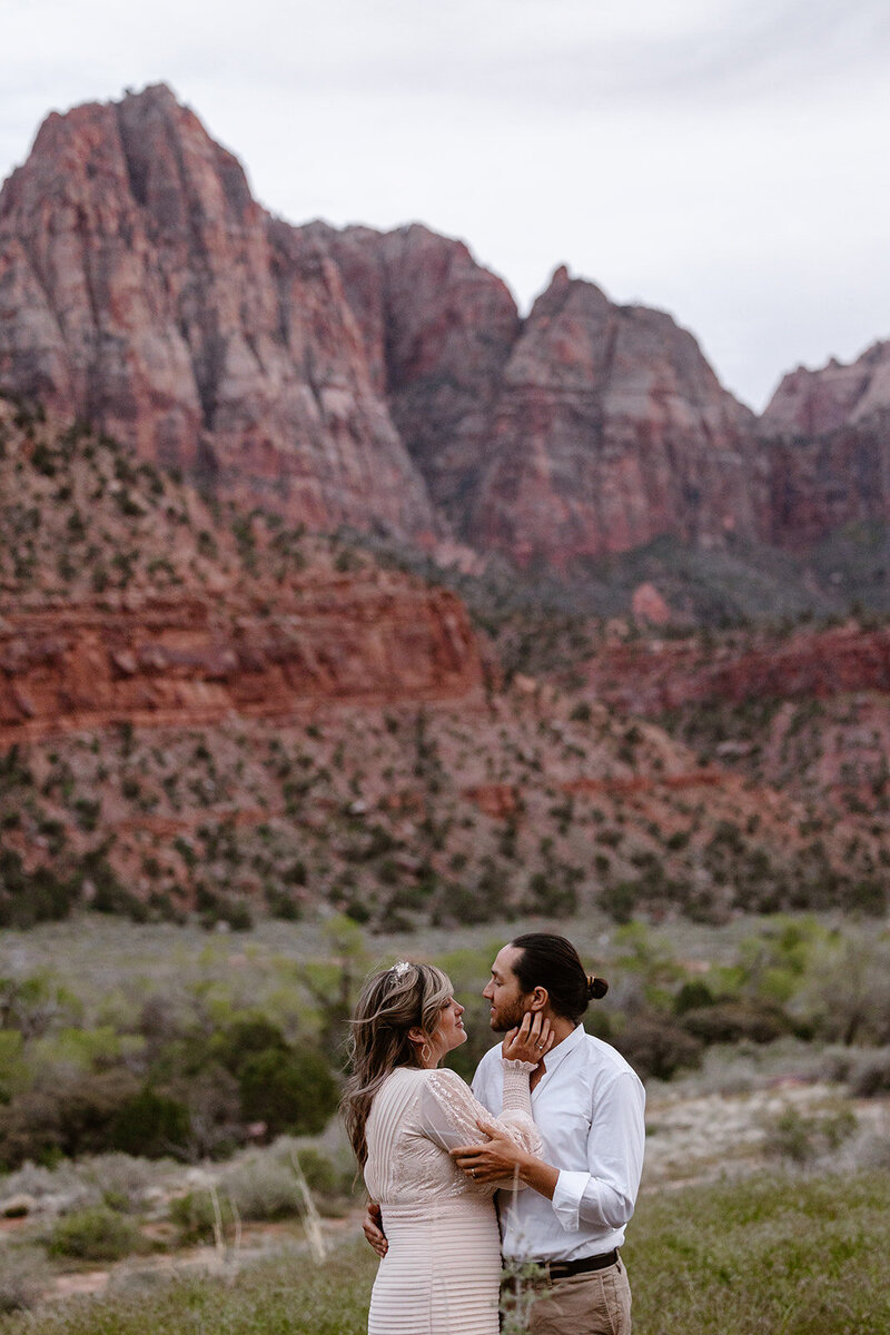 A couple in front of the red rocks of Utah. The bride is gently touching the cheek of her groom. 