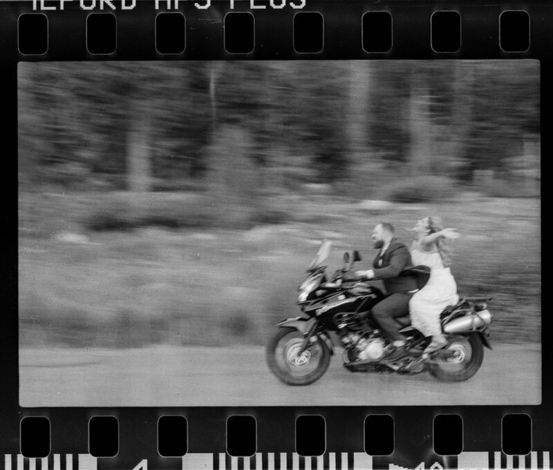 black and white film photo of a wedding couple riding a motorcycle