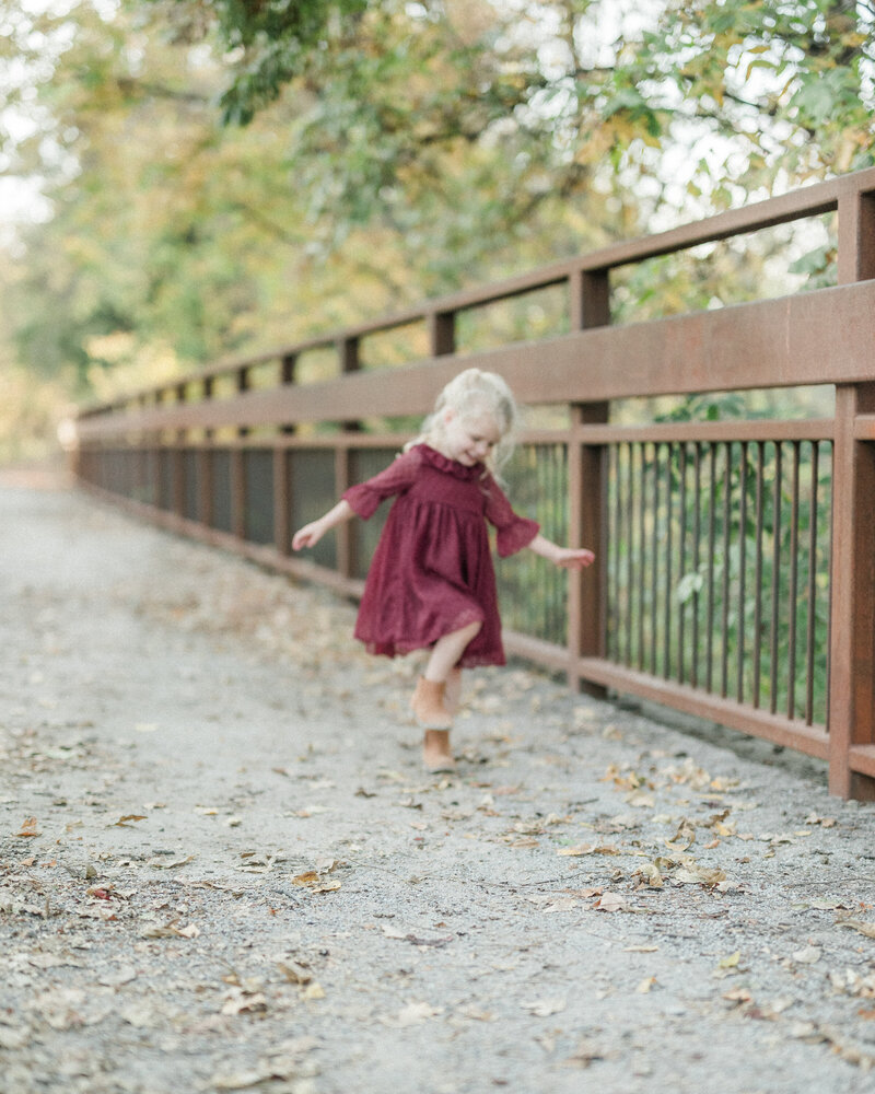 Young girl running joyfully across a rustic wooden bridge during a lifestyle family session in Kansas City.