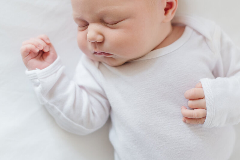Newborn baby asleep in a white long sleeve onesie - Washington DC Newborn Photographer