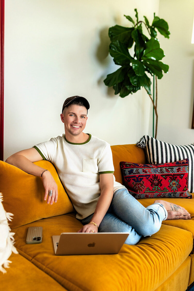 Madison Wetter standing in a bright kitchen with a warm smile. He is wearing a maroon baseball cap and an off-white knit sweater.