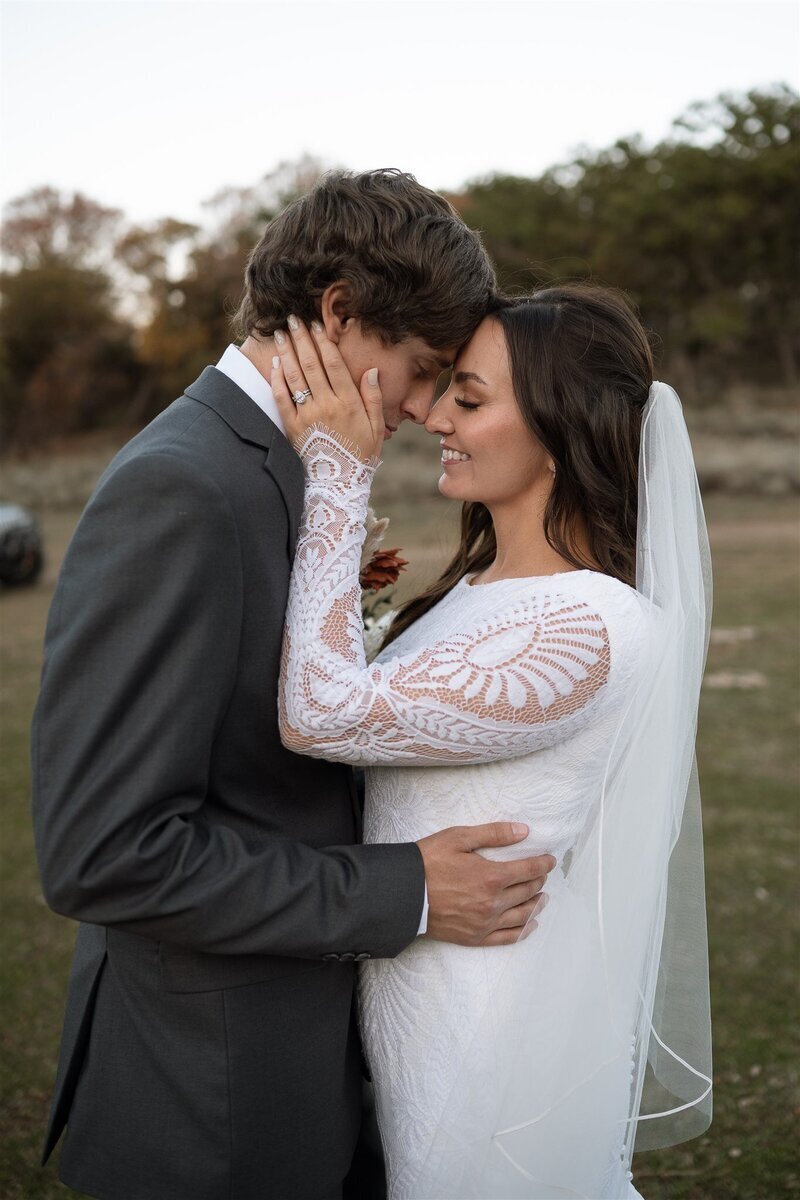 Close up portrait of bride and groom. Groom is wearing a grey suit while the bride is in white with intricate patterns on sleeves.