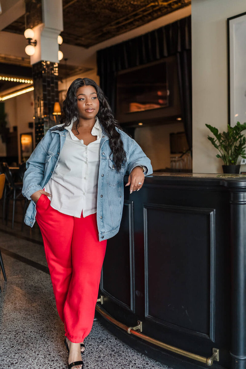 Bipoc woman in red sweatpants and heels leaning on 