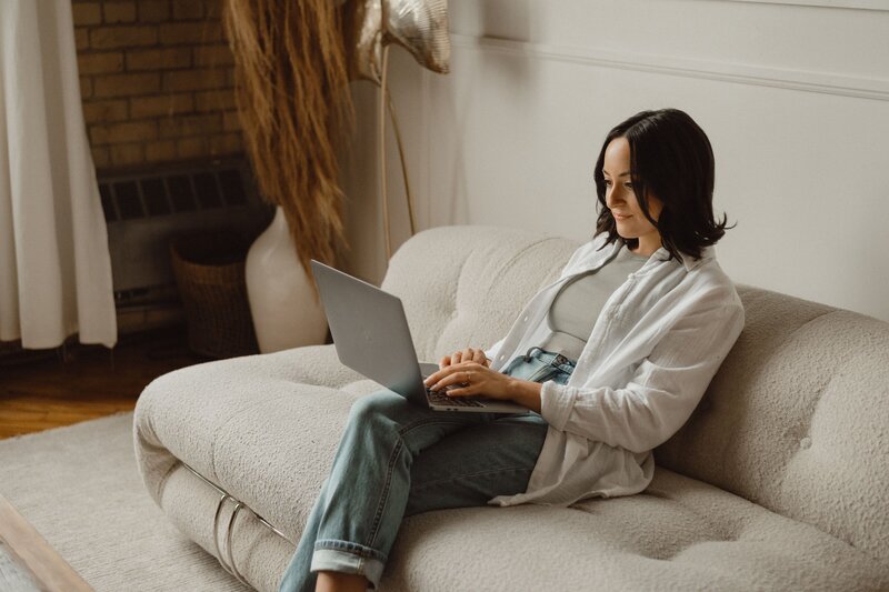 MacBook on a white table with peach-colored flowers in a gold watering can, creating a calming and professional workspace for wellness professionals.