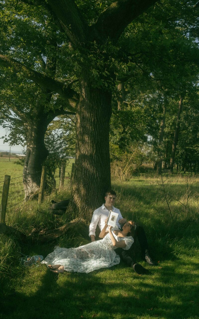 A peaceful and intimate moment of a couple laying on the grass under the shade of a tree, enjoying each other's company in a tranquil setting