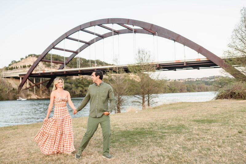 Couple go for a walk along the Colorado River during their engagement session at the 360 bridge in Austin, Texas. Photo taken by Austin Engagement Photographers, Joanna & Brett Photography
