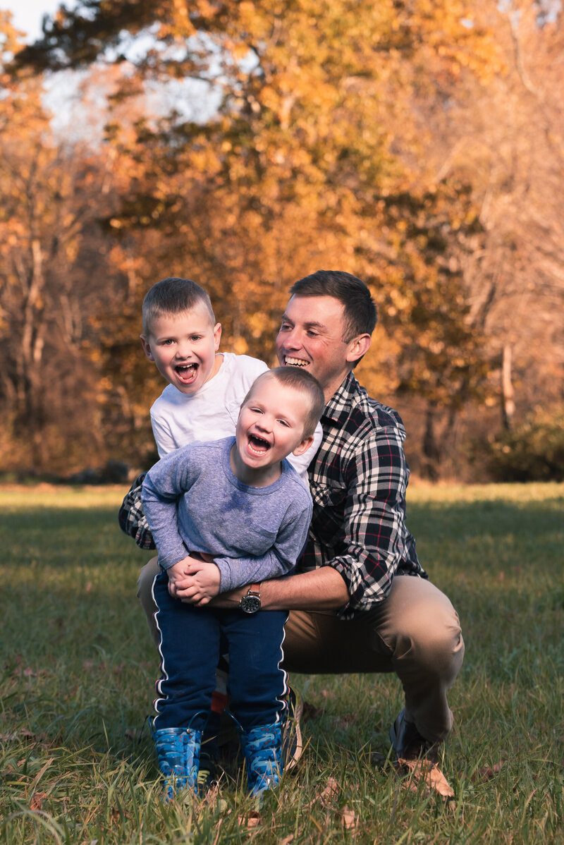 dad laughing with two sons on farm near boston during family photo shoot