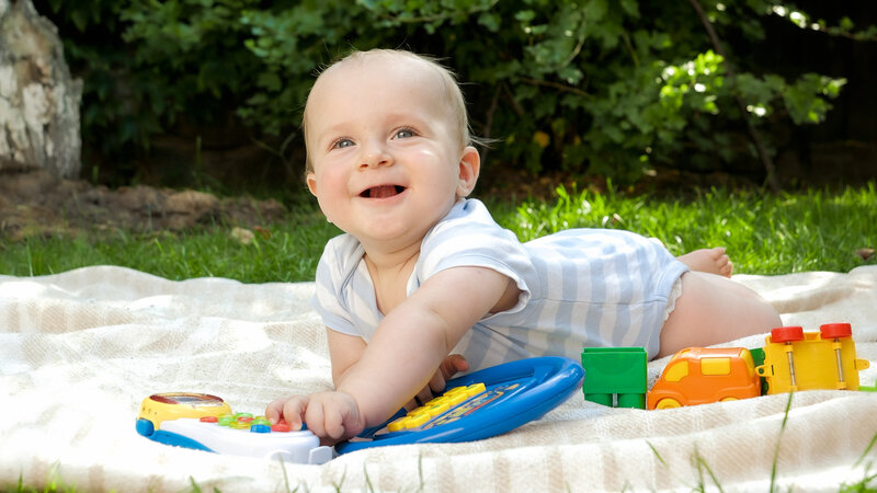 baby laying on a blanket outside smiling and playing with toys