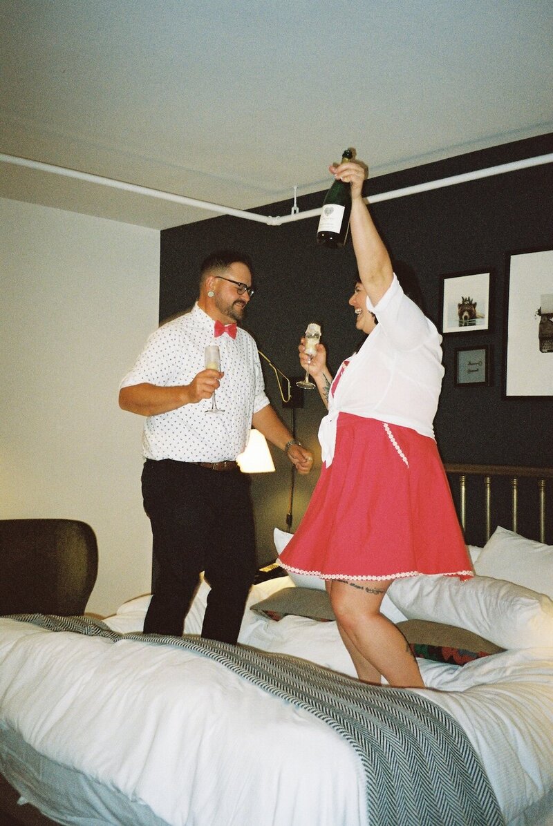 Engaged couple dancing and laughing on a hotel bed during a playful Fort Collins, Colorado engagement session captured on 35mm film.