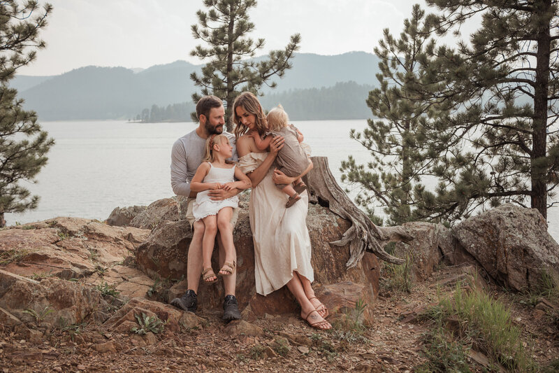 Jaime and Lenci, the owners of the August House wedding venue, are seated on rocks by a picturesque North Dakota lake with their two young children, illustrating the warm family atmosphere of this Dickinson, ND wedding venue.