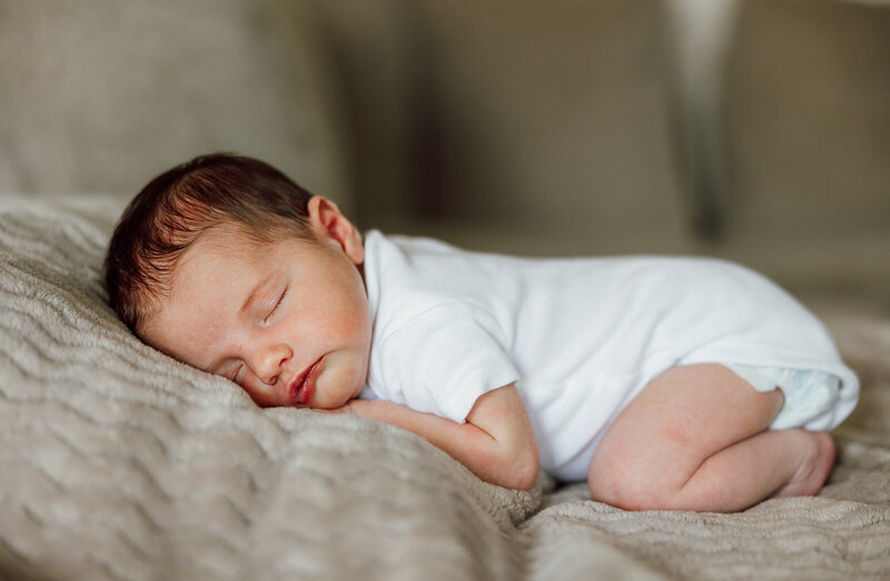 A sleeping infant laying on her stomach while wearing a white onesie taken in the living room in Hillsboro, Missouri. 