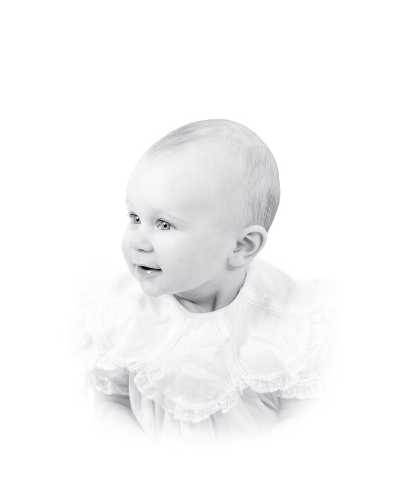 Black and white heirloom portrait of a smiling baby dressed in a classic white outfit with lace details. This timeless baby photography captures the innocence and joy of childhood, created by a Birmingham newborn photographer specializing in elegant, light-filled portraits.