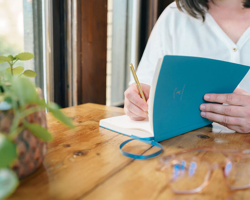 Kat Jackson writing in a blue notebook to customize SEO website copywriting options for a client.