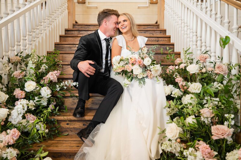 Bride and groom sit on the stairs surrounded by florals at Walker Farms
