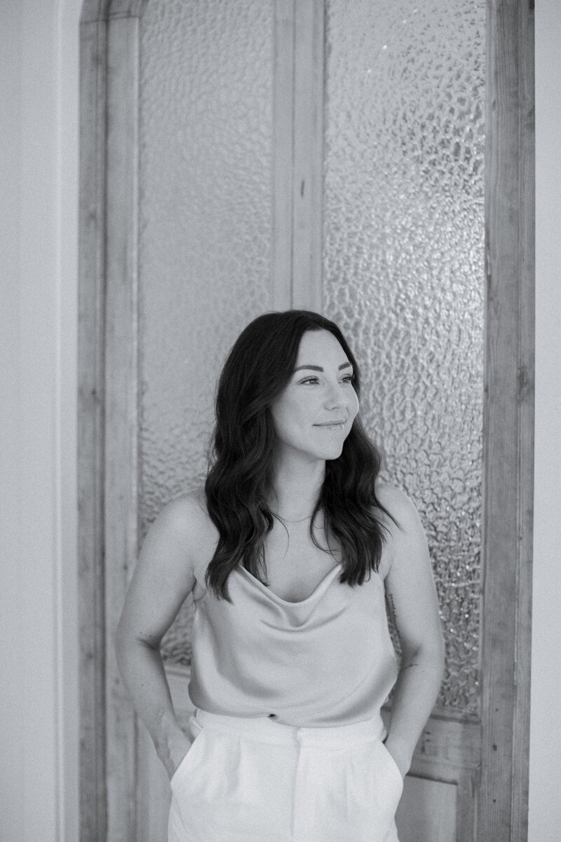 Woman standing in front of glass and wood door looking off camera
