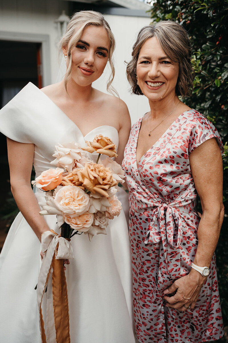 Bella Rae Bride Kristen with a beautiful low bun and curled face framing and soft glam makeup standing with her mum who has soft waves and beautiful soft bronzed makeup. Picture taken  by Daniel Charfer Photography at Austinvilla Estate