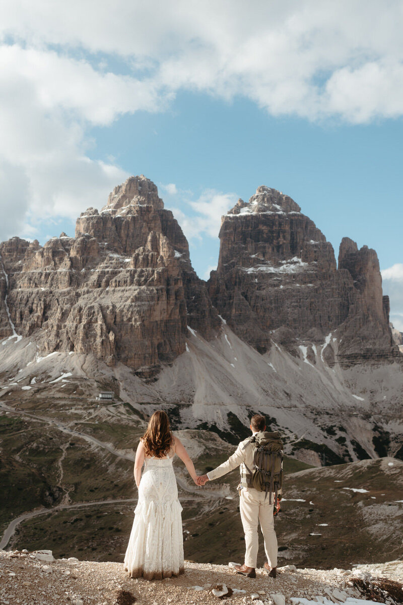 Bride and groom having a hiking wedding, holding hands in front of a massive mountain 