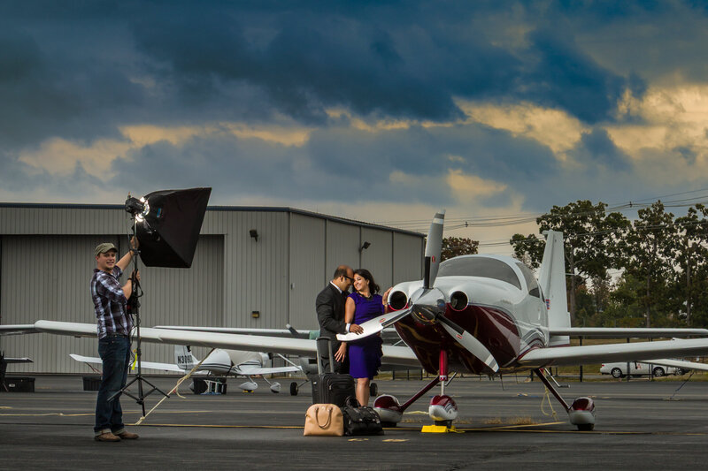 Travis Stitt with an engaged couple at a small private airport, posing beside a private plane during a jet-set engagement session, capturing their adventurous spirit and the allure of luxury travel.