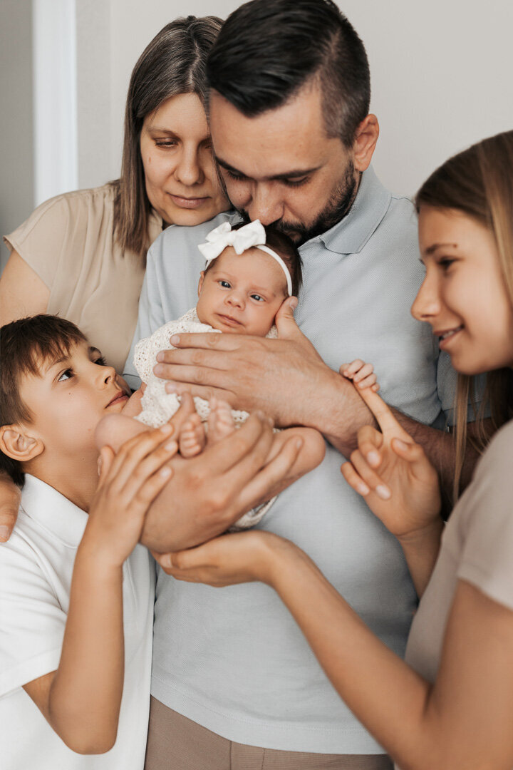 Newborn baby girl cradled by her father while surrounded by loving family members during an in-home lifestyle session in Las Vegas with Angela Wolf Photography