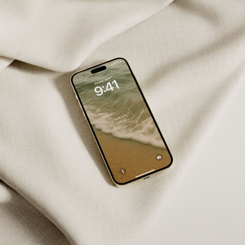 iPhone on a soft neutral fabric, featuring an inspirational lock screen wallpaper that reads, ‘Inhale Exhale’