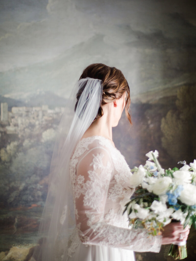 Bride in lace dress holding spring bouquet of lavender and eucalyptus in white and blue with groom in black tuxedo at Cornman Farms